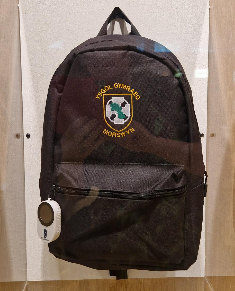 A black children's school backpack with an air quality monitoring device clipped onto it.